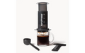 Black aeropress kahvinvalmistuslaite läpinäkyvällä mäntällä ja mittamerkinnöillä varustetulla lasimukilla