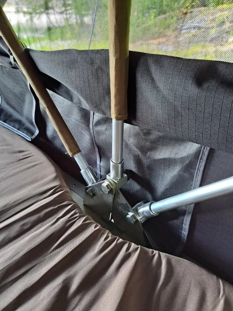 Silverinen metallinen telttakeppi puisella kahvalla kiinnitettynä mustan auton kattoteltan kehykseen
