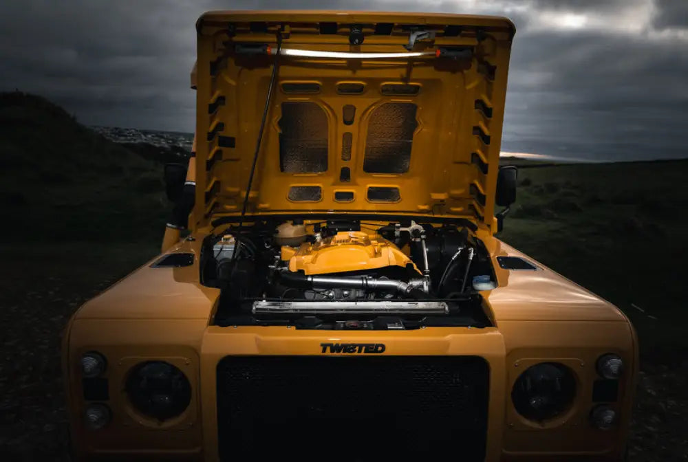 Keltainen land rover defender avoimella konepellillä, esittelee räätälöidyn moottoritilan ja twisted-brändin bando 1k strap light työvalo