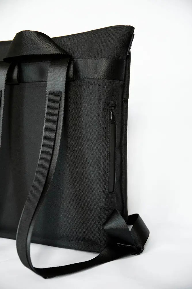 Musta nylon hölär säänkestävä reppu säädettävillä olkahihnoilla ja sivuvetoketjutaskulla näkymä takaa