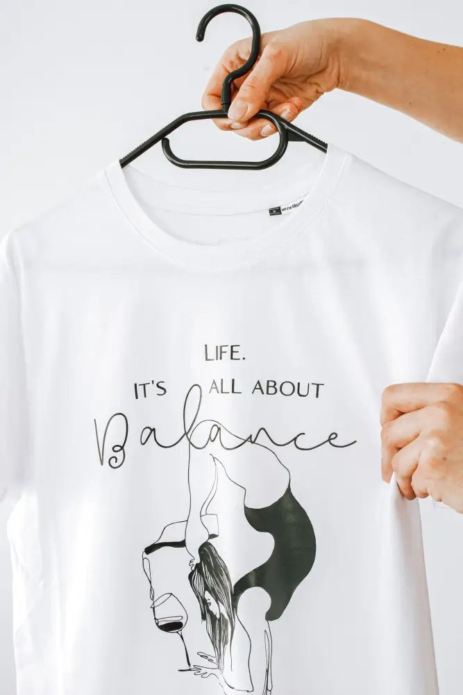 Valkoinen puuvillainen t-paita jossa musta viivapiirros naisesta jooga-asennossa ja teksti life on it’s all about balance t-paita