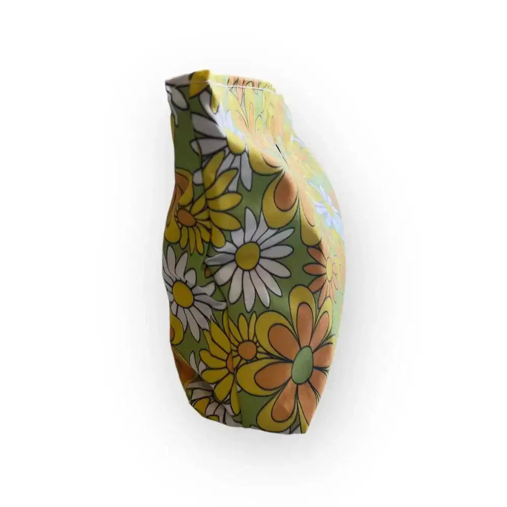 Meikkilaukku rentukka with a glossy ceramic vase featuring bold yellow white orange and green daisies on olive background