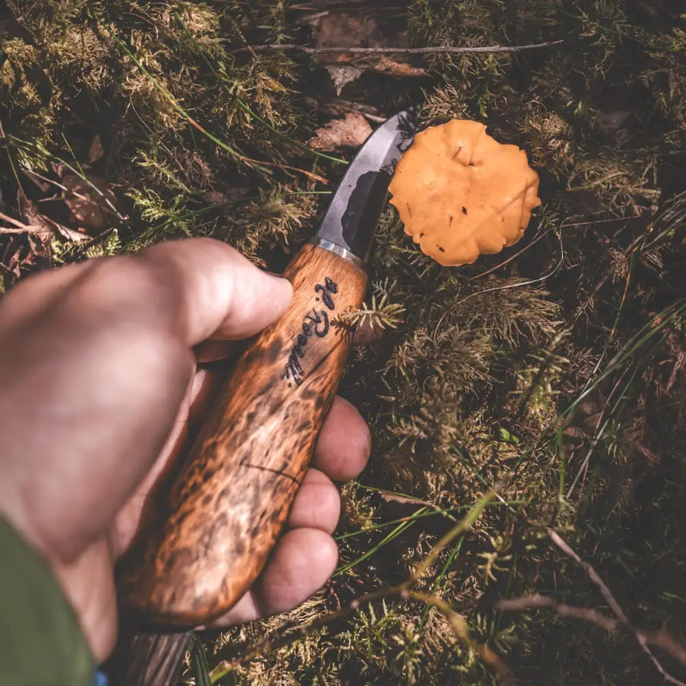 A handcrafted wooden-handled mushroom knife with a blackened steel blade and engraved lettering on the handle