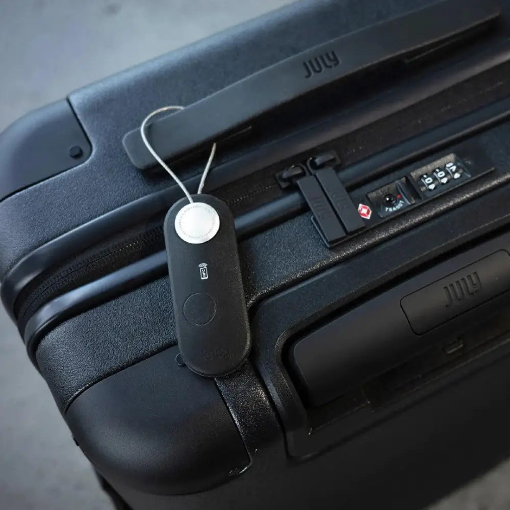 Musta suorakulmainen scout travel black matkalaukun merkintätarra hopealla pyöreällä napilla ja july-logolla