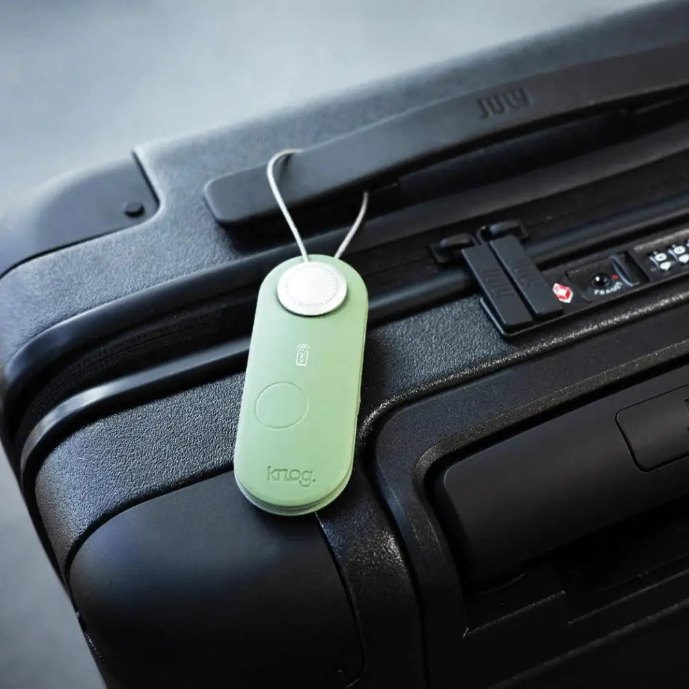 A sleek matte sage green knog luggage tag with a circular silver button from Scout Travel Green collection